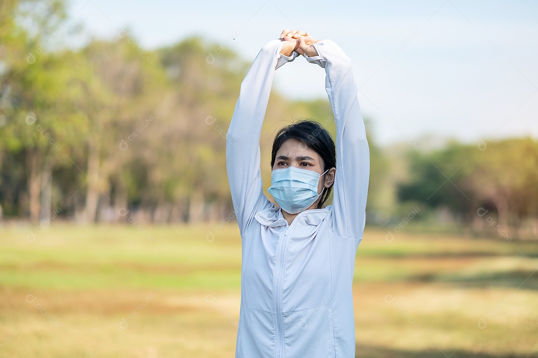 Mulher adulta jovem usando máscara facial protetora durante o alongamento muscular no parque ao ar livre