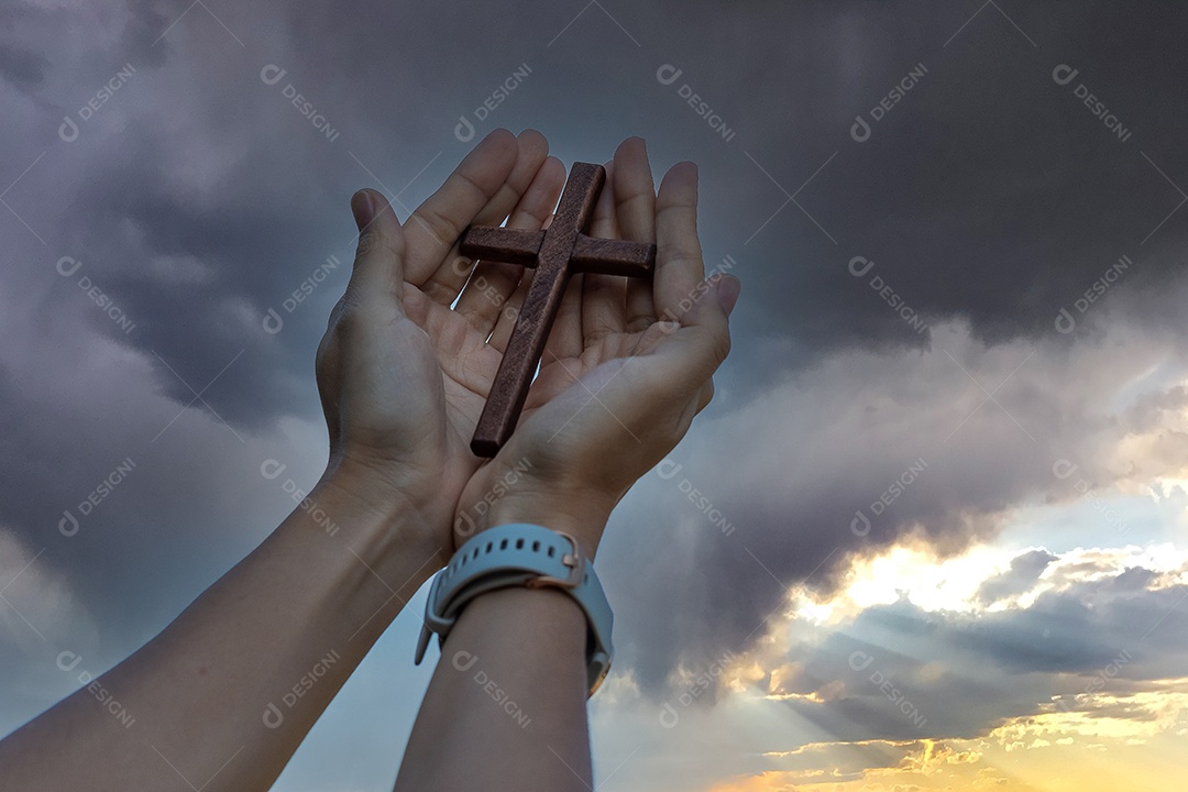Silhueta mão segurando a cruz de madeira contra o fundo do nascer do sol, palma aberta para cima adoração, orar por bênçãos de Deus