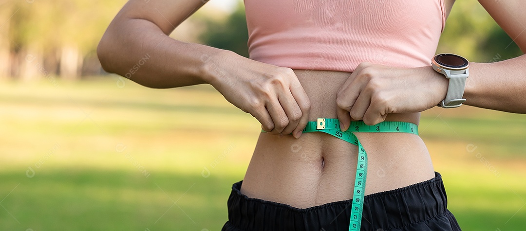 Fêmea jovem de corpo magro em roupas esportivas rosa, mulher saudável, medindo sua cintura fina com uma fita métrica no parque ao ar livre
