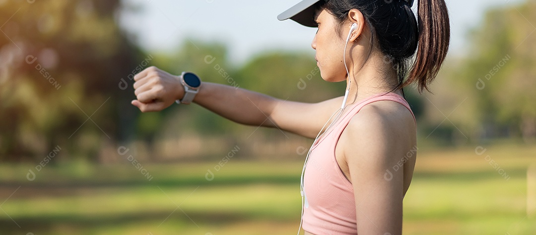 Mulher adulta jovem, verificando o tempo e a frequência cardíaca cardio no smartwatch esportivo durante a corrida no parque ao ar livre