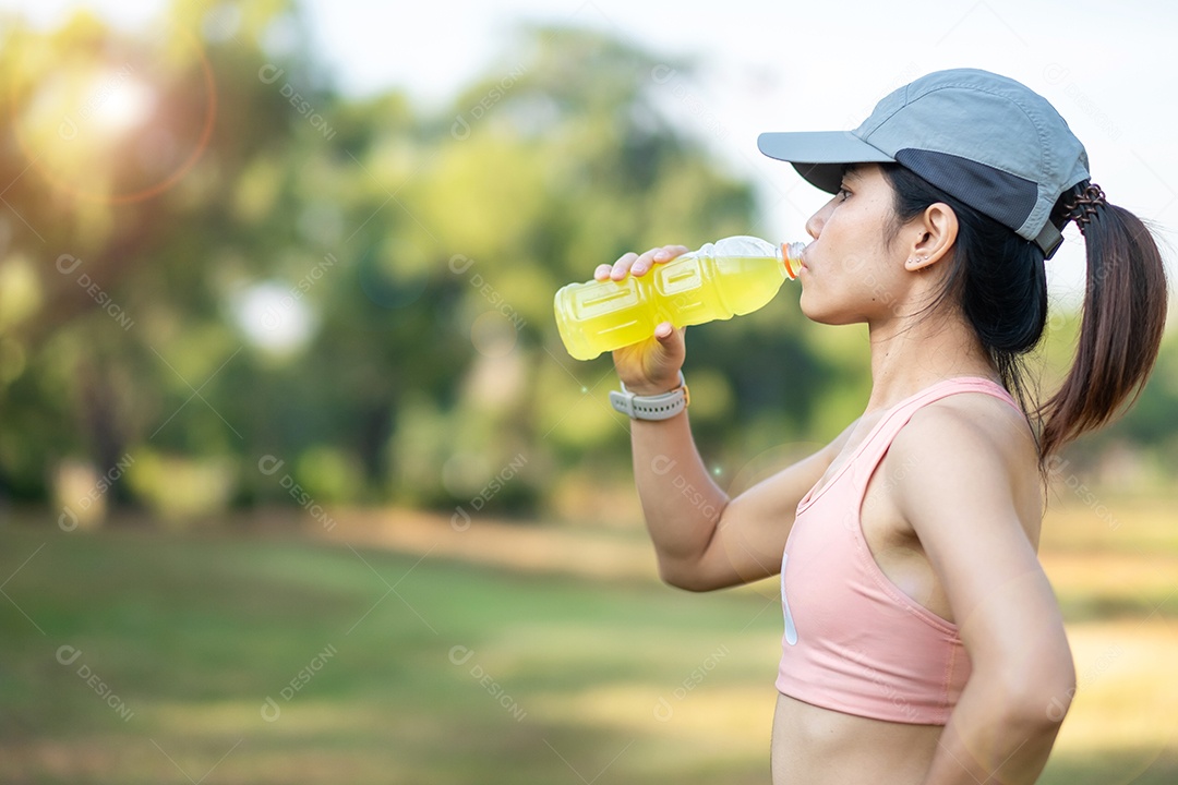 mulher jovem fitness bebendo água energética durante o alongamento muscular no parque ao ar livre, atleta asiático correndo e se exercitando de manhã