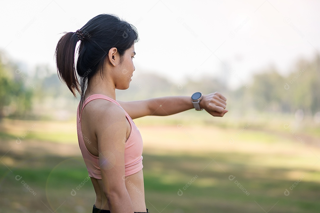 Mulher adulta jovem, verificando o tempo e a frequência cardíaca cardio no smartwatch esportivo durante a corrida no parque ao ar livre