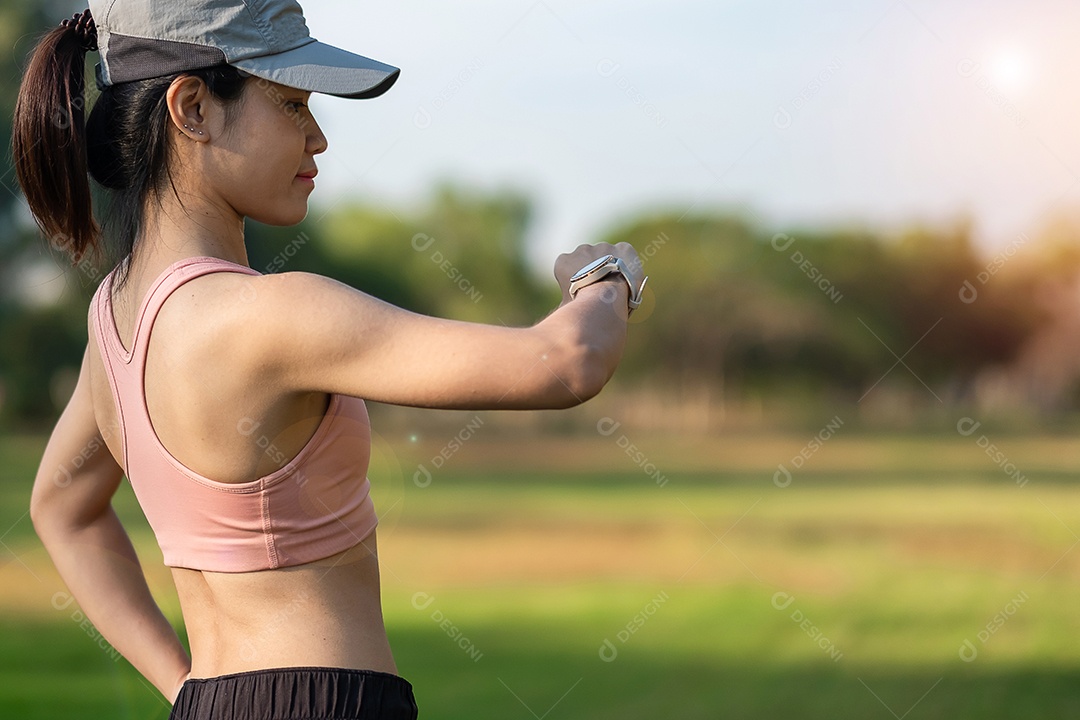Mulher adulta jovem, verificando o tempo e a frequência cardíaca cardio no smartwatch esportivo durante a corrida no parque ao ar livre, mulher corredora