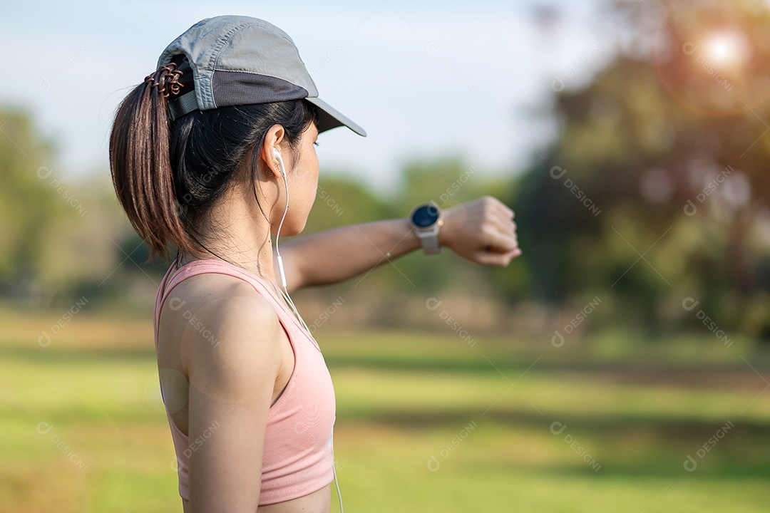 Mulher adulta jovem, verificando o tempo e a frequência cardíaca cardio no smartwatch esportivo durante a corrida no parque ao ar livre, mulher corredora