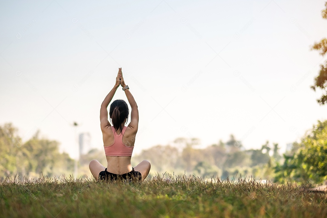 Mulher adulta jovem em roupas esportivas fazendo Yoga no parque ao ar livre, mulher saudável sentada na grama e meditação com pose de lótus de manhã