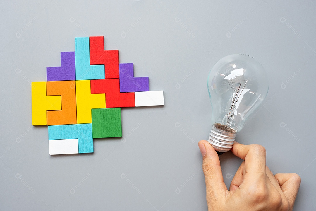 Hand holding light bulb with colorful wooden puzzle piece on gray background. New idea, creativity, innovation, imagination