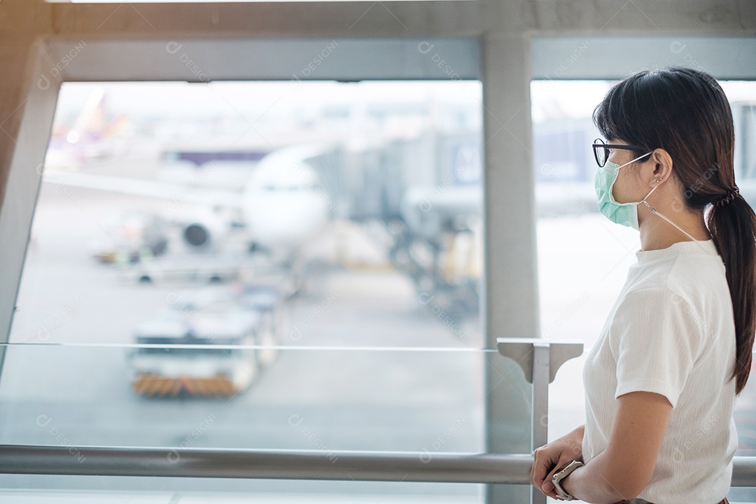 Jovem mulher usando máscara facial e usando smartphone móvel no aeroporto, proteção contra infecção por doença de coronavírus (Covid-19). Novo normal e distanciamento social