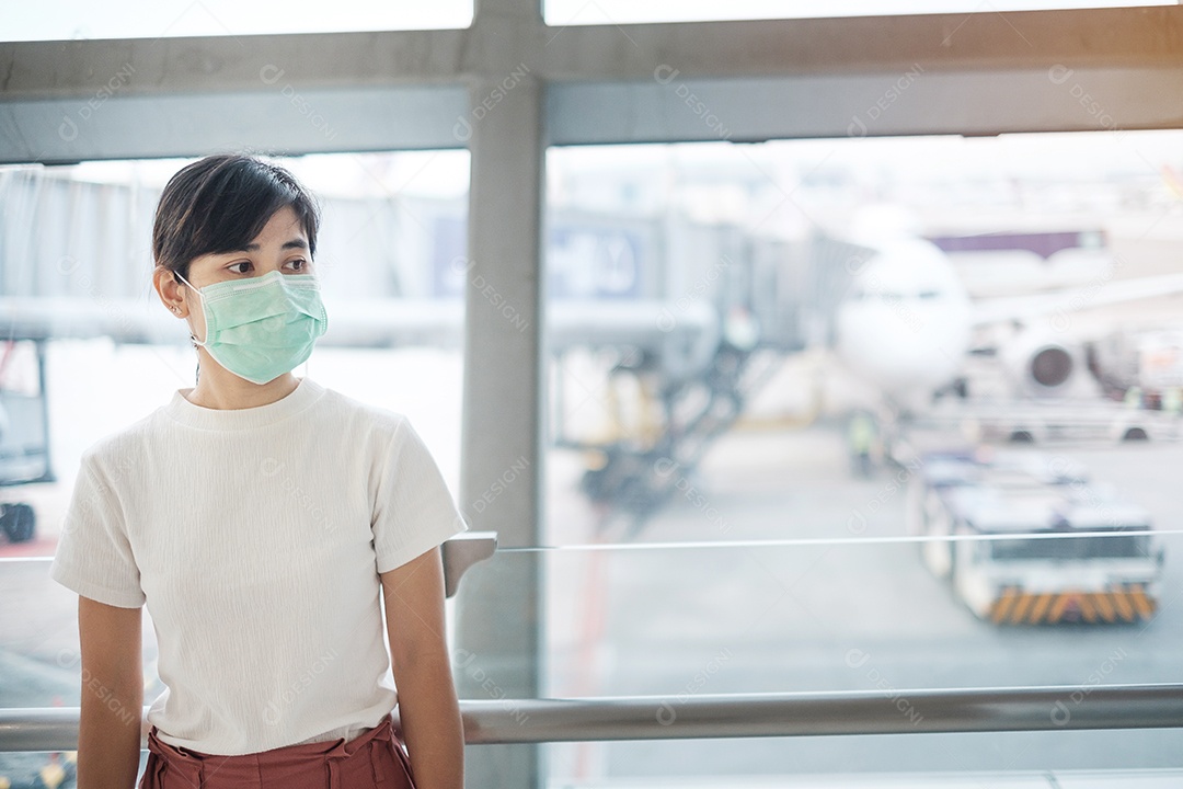 Young woman wearing face mask and using mobile smartphone at airport, protection from coronavirus disease (Covid-19) infection. New normal and social distancing