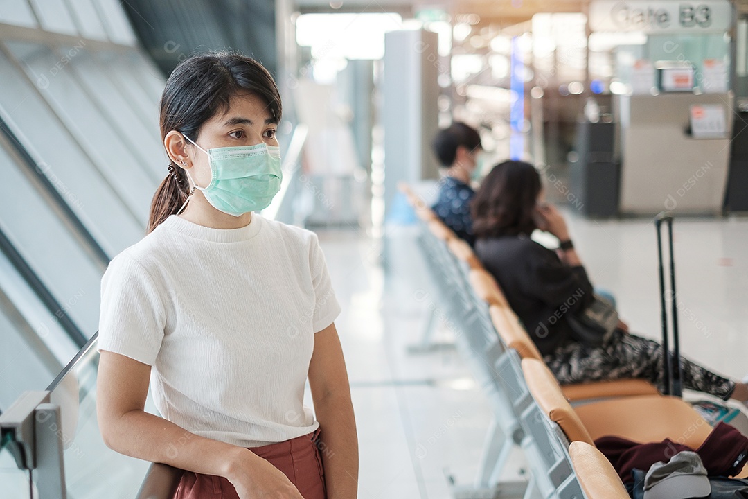 Jovem mulher usando máscara facial e usando smartphone móvel no aeroporto, proteção contra infecção por doença de coronavírus (Covid-19). Novo normal e distanciamento social
