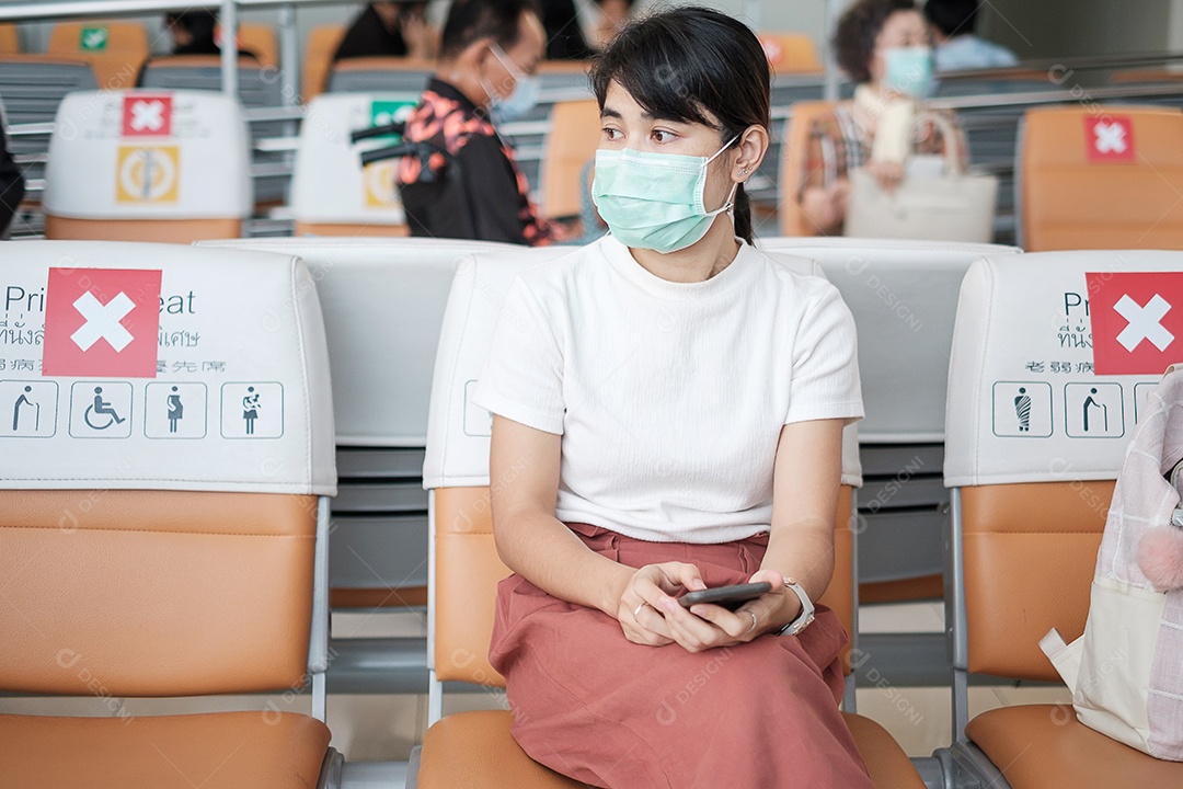 Jovem mulher usando máscara facial e usando smartphone móvel no aeroporto, proteção contra infecção por doença de coronavírus (Covid-19). Novo normal e distanciamento social