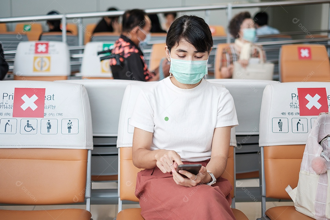 Jovem mulher usando máscara facial e usando smartphone móvel no aeroporto, proteção contra infecção por doença de coronavírus (Covid-19). Novo normal e distanciamento social