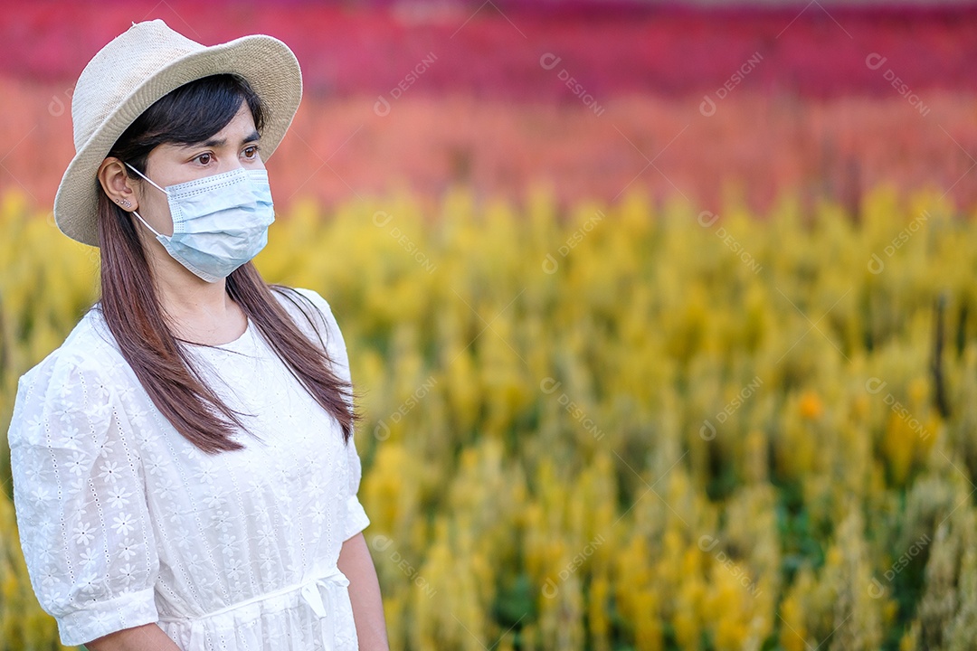 Mulher turista feliz usando máscara facial cirúrgica desfruta de belo jardim de flores, proteção contra infecção por doença de coronavírus