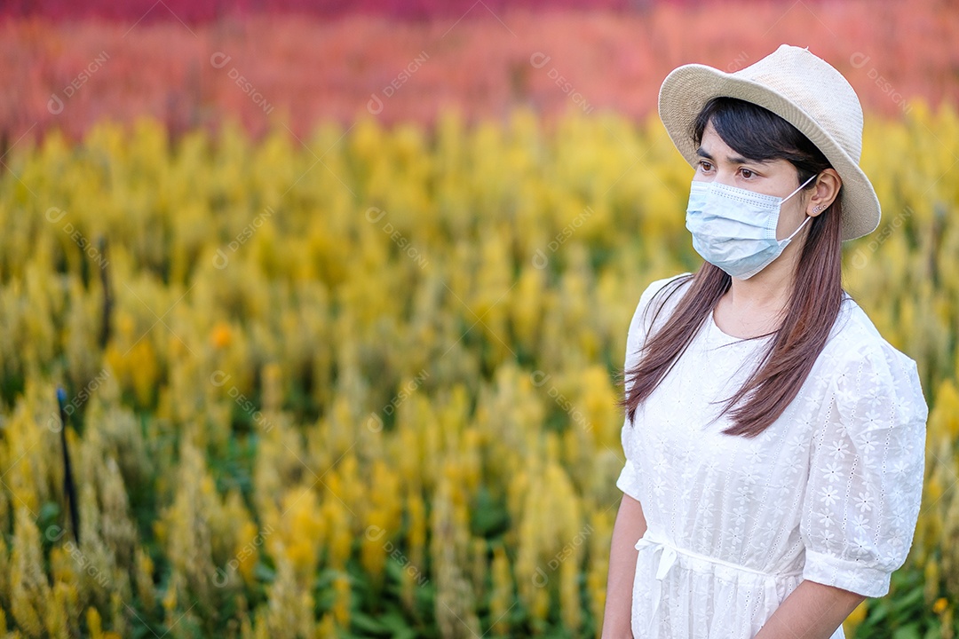 Mulher turista feliz usando máscara facial cirúrgica desfruta de belo jardim de flores, proteção contra infecção por doença de coronavírus