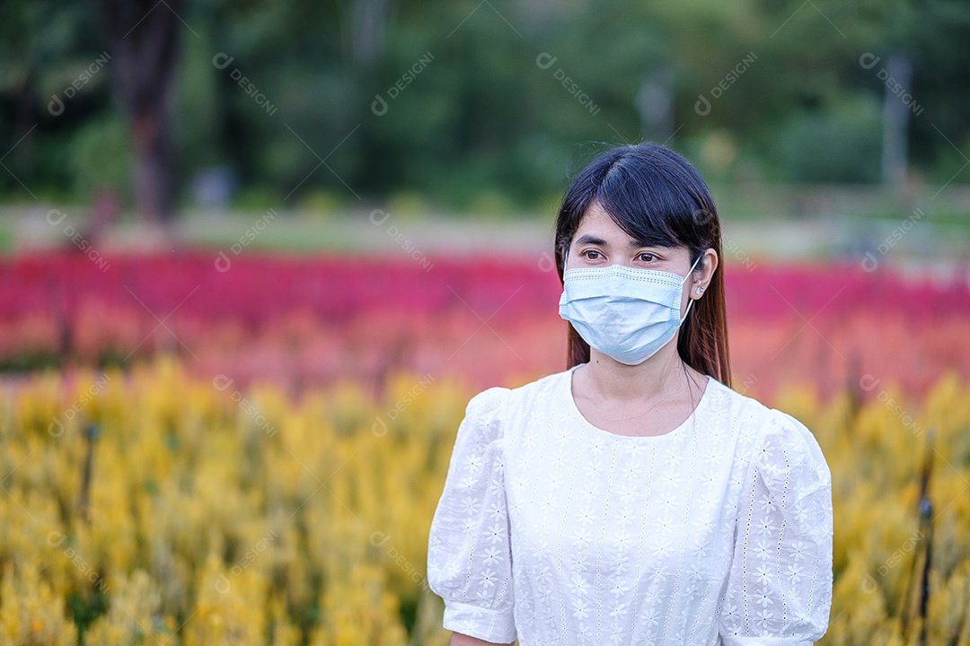 Mulher turista feliz usando máscara facial cirúrgica desfruta de belo jardim de flores, proteção contra infecção por doença de coronavírus