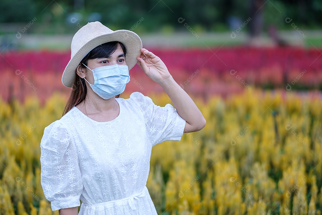 Mulher turista feliz usando máscara facial cirúrgica desfruta de belo jardim de flores, proteção contra infecção por doença de coronavírus