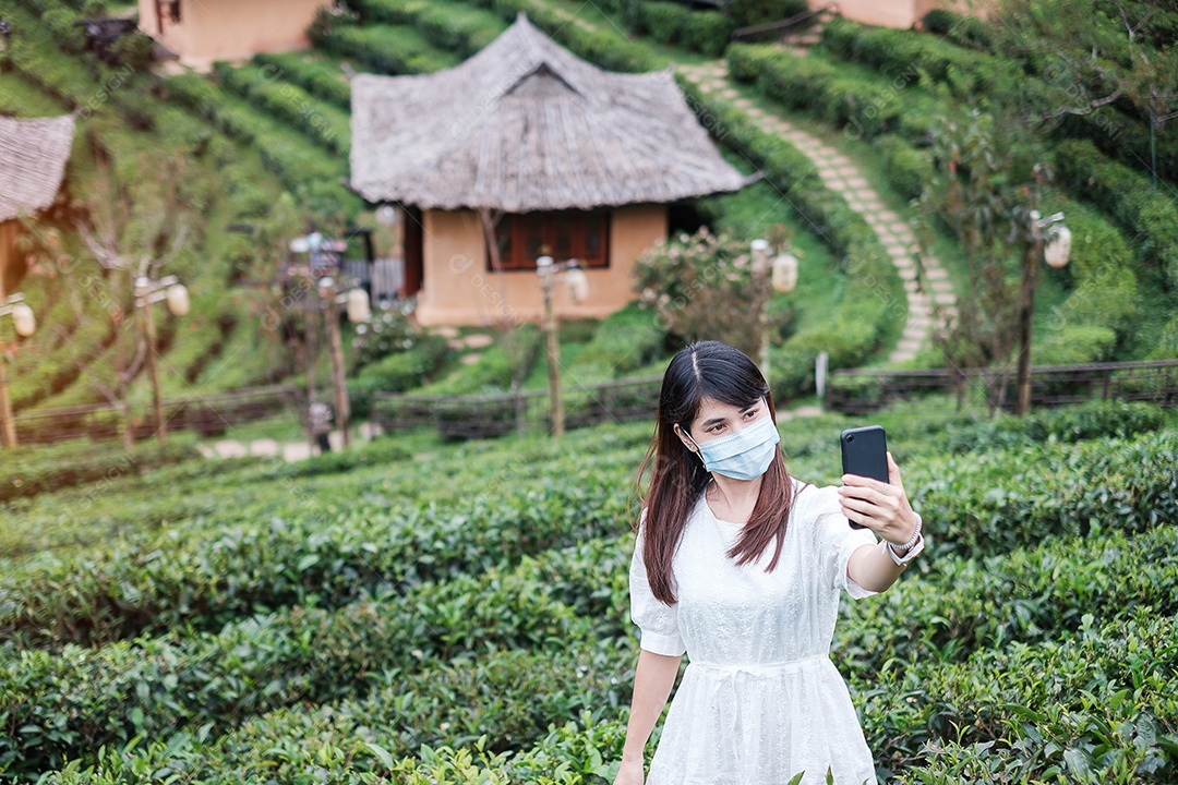 Mulher turista feliz usando máscara facial cirúrgica desfruta de um belo jardim de chá, proteção contra infecção por doença de coronavírus