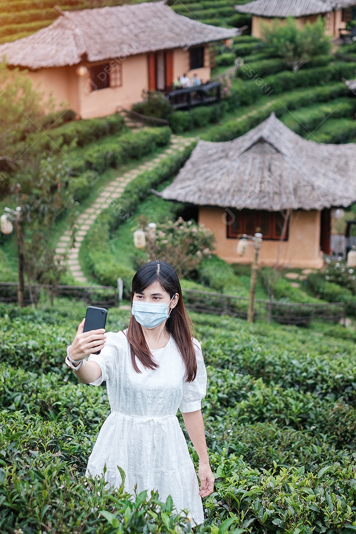 Mulher turista feliz usando máscara facial cirúrgica desfruta de um belo jardim de chá, proteção contra infecção por doença de coronavírus