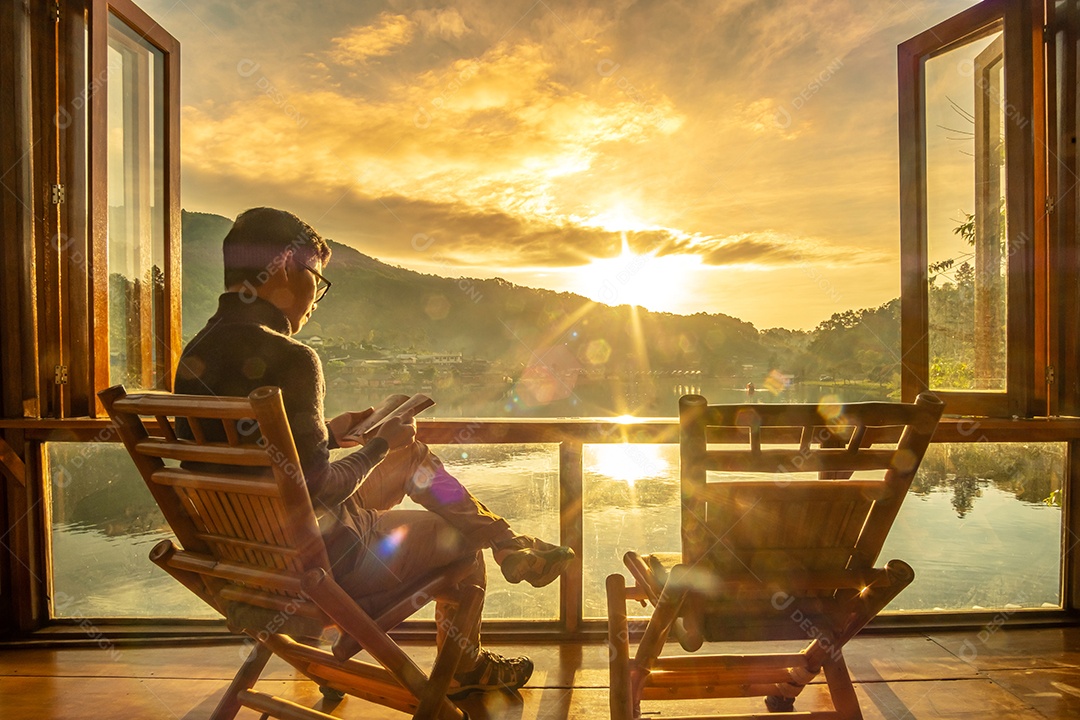 jovem lendo livro perto da janela e assistindo a vista para o lago no café ao nascer do sol da manhã, vila tailandesa de Ban Rak, província de Mae Hong Son, Tailândia. Conceito de viagem