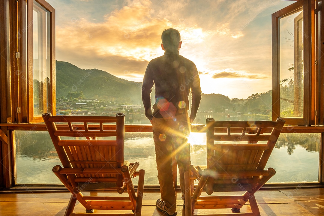 Jovem feliz assistindo a vista para o lago no café ao nascer do sol da manhã, vila de Ban Rak Thai, província de Mae Hong Son, Tailândia. Conceito de viagem