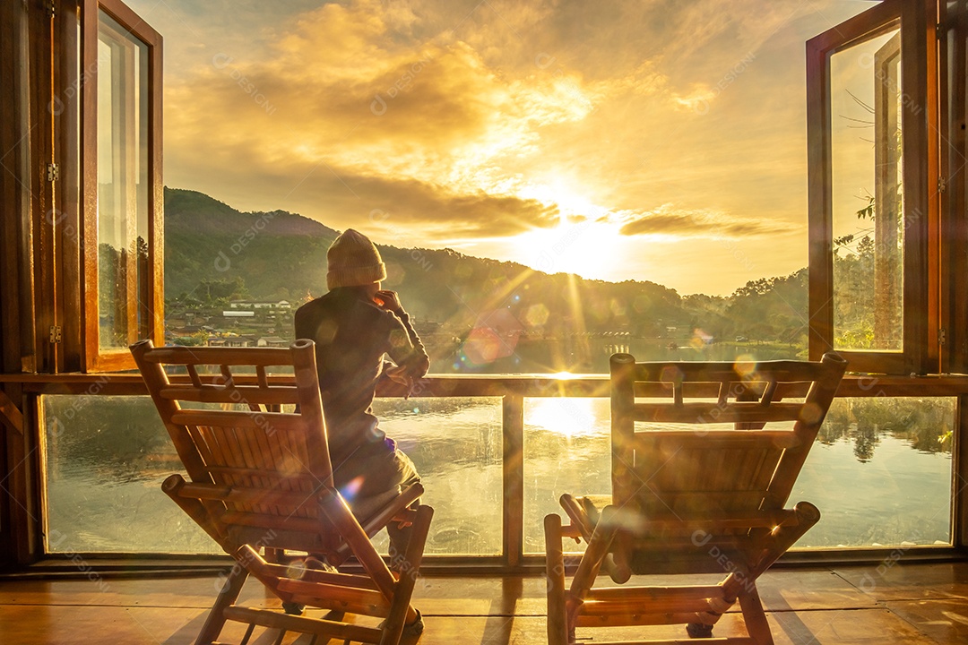 jovem mulher sozinha assistindo a vista para o lago no café ao nascer do sol da manhã, vila de Ban Rak Thai, província de Mae Hong Son, Tailândia. Conceito de viagem
