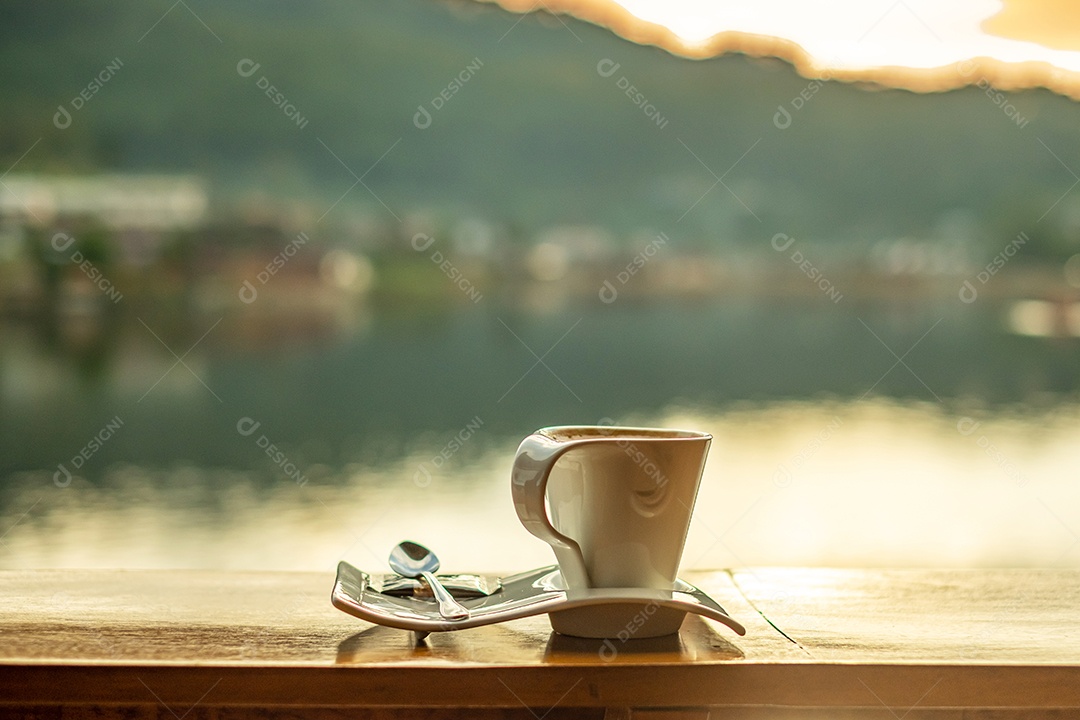 xícara de café quente na mesa de madeira contra o fundo de vista para o lago na cafeteria ao nascer do sol da manhã