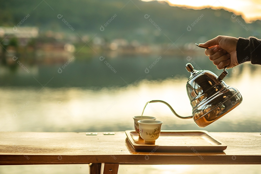 xícara de café quente na mesa de madeira contra o fundo de vista para o lago na cafeteria ao nascer do sol da manhã