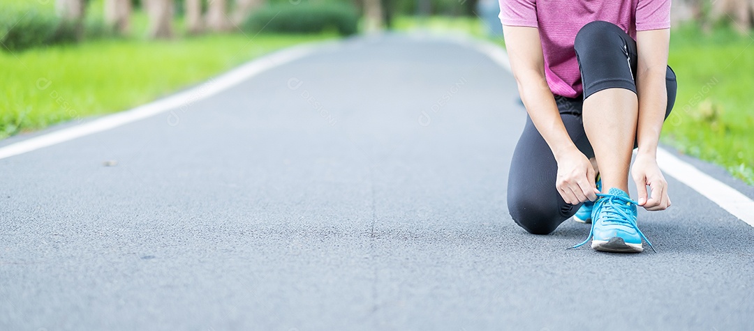 Mulher adulta jovem em roupas esportivas amarrando cadarço no parque.