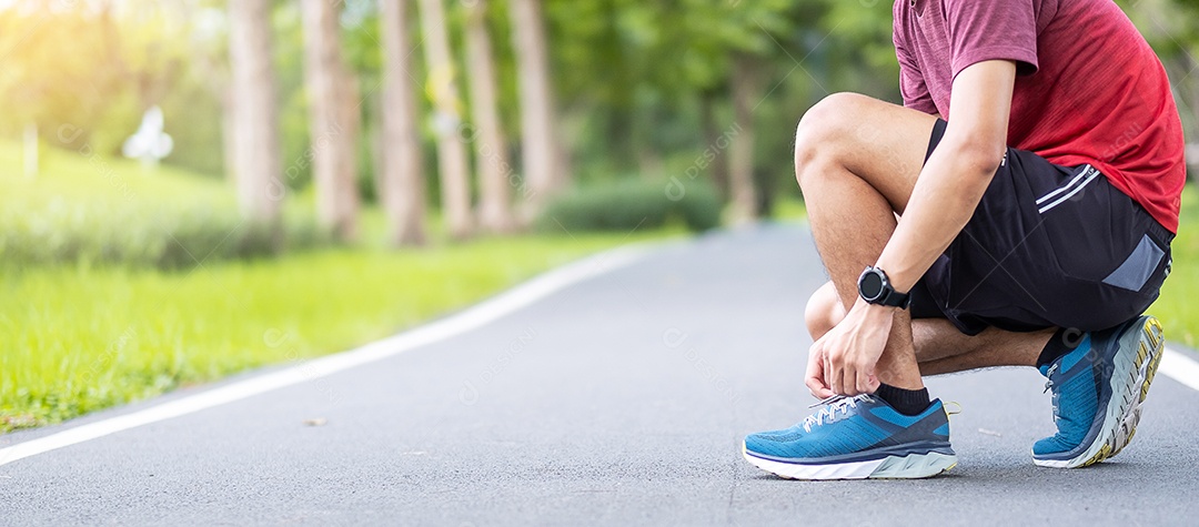 Macho adulto jovem em roupas esportivas e smartwatch amarrando cadarço.