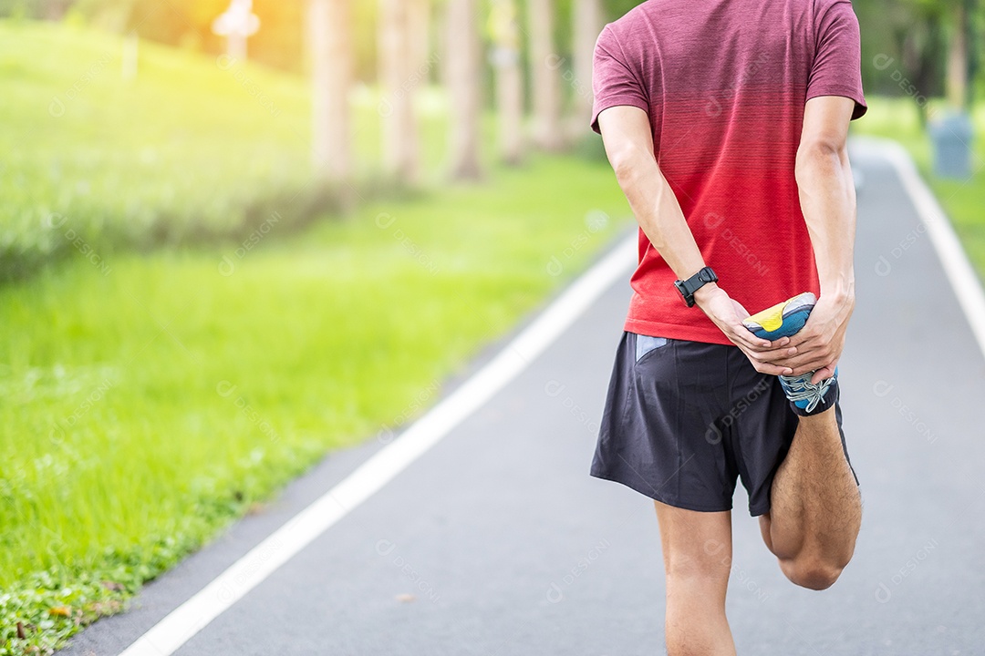 Macho adulto jovem em roupas esportivas vermelhas esticando o músculo no parque.