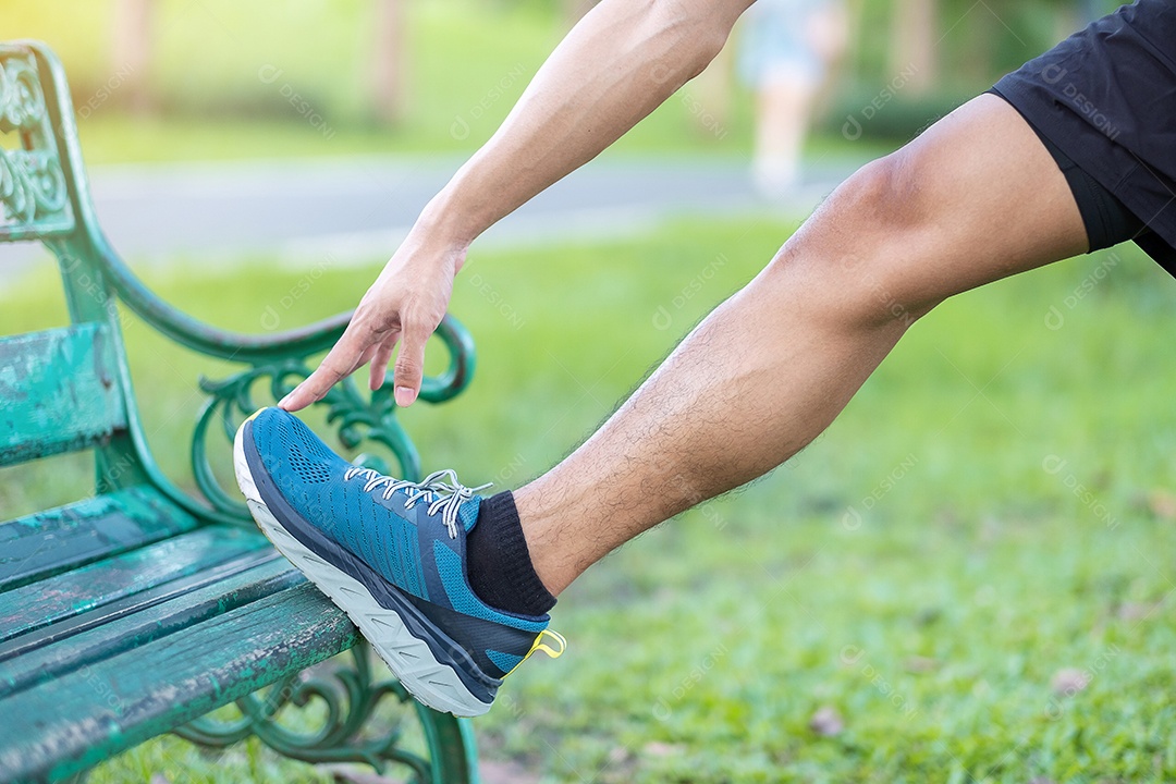 Macho adulto jovem em roupas esportivas vermelhas esticando o músculo no parque.