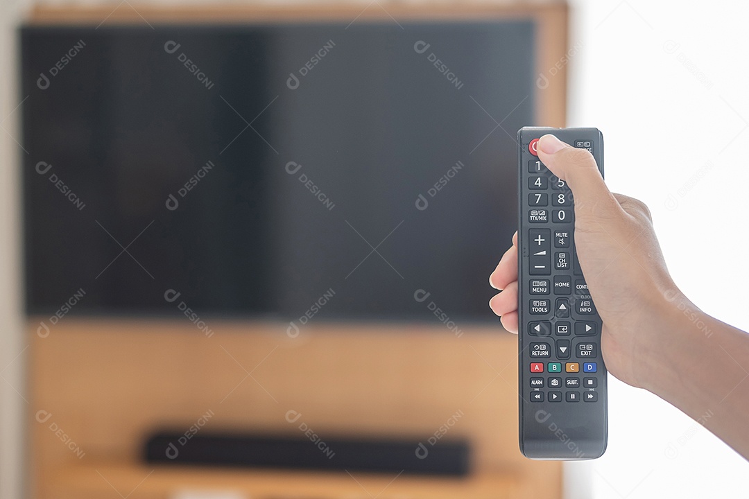 Mão usando o controle remoto para ajustar a Smart TV dentro da sala moderna em casa ou hotel de luxo