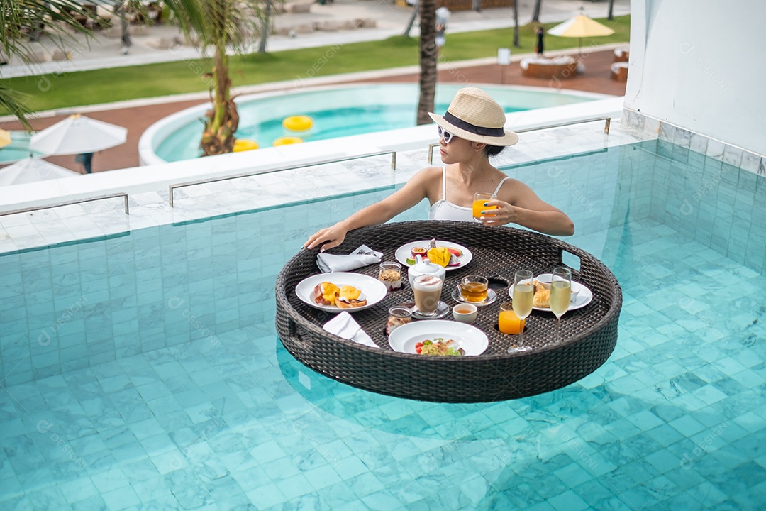 Happy woman in white swimsuit with floating breakfast tray at luxury pool hotel, young woman with sunglasses enjoys in tropical resort. Relaxing, exotic summer travel, vacation, vacation and weekend