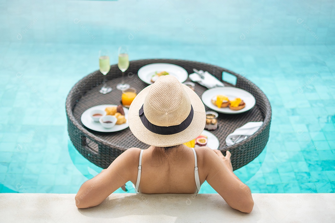 Mulher feliz em maiô branco com bandeja de café da manhã flutuante no hotel de piscina de luxo, jovem fêmea com chapéu desfrutar em resort tropical. Relaxante, viagens de verão exóticas, férias, férias e fim de semana