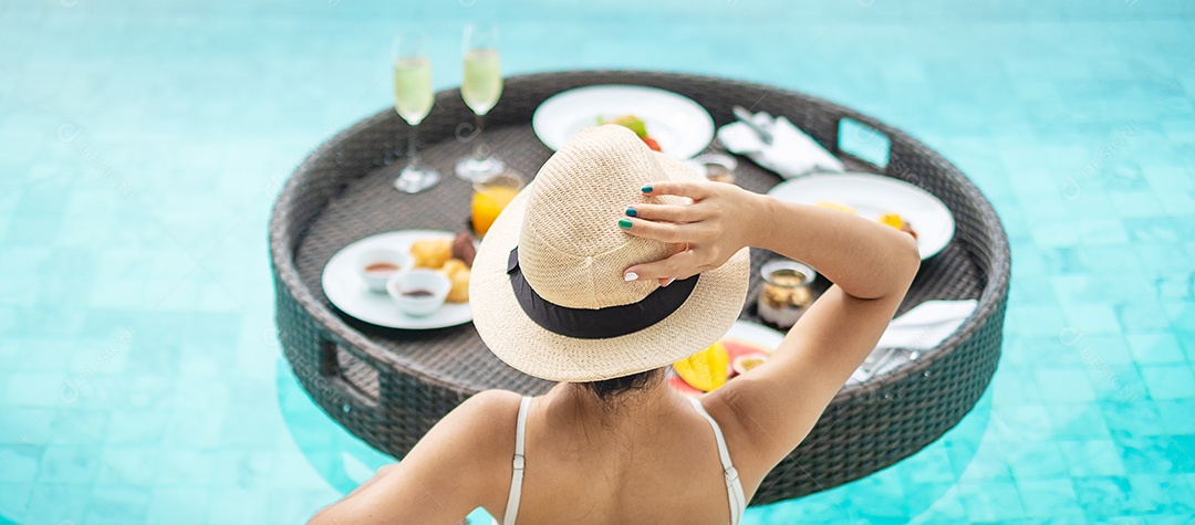 Mulher feliz em maiô branco com bandeja de café da manhã flutuante no hotel de piscina de luxo, jovem fêmea com chapéu desfrutar em resort tropical. Relaxante, viagens de verão exóticas, férias, férias e fim de semana