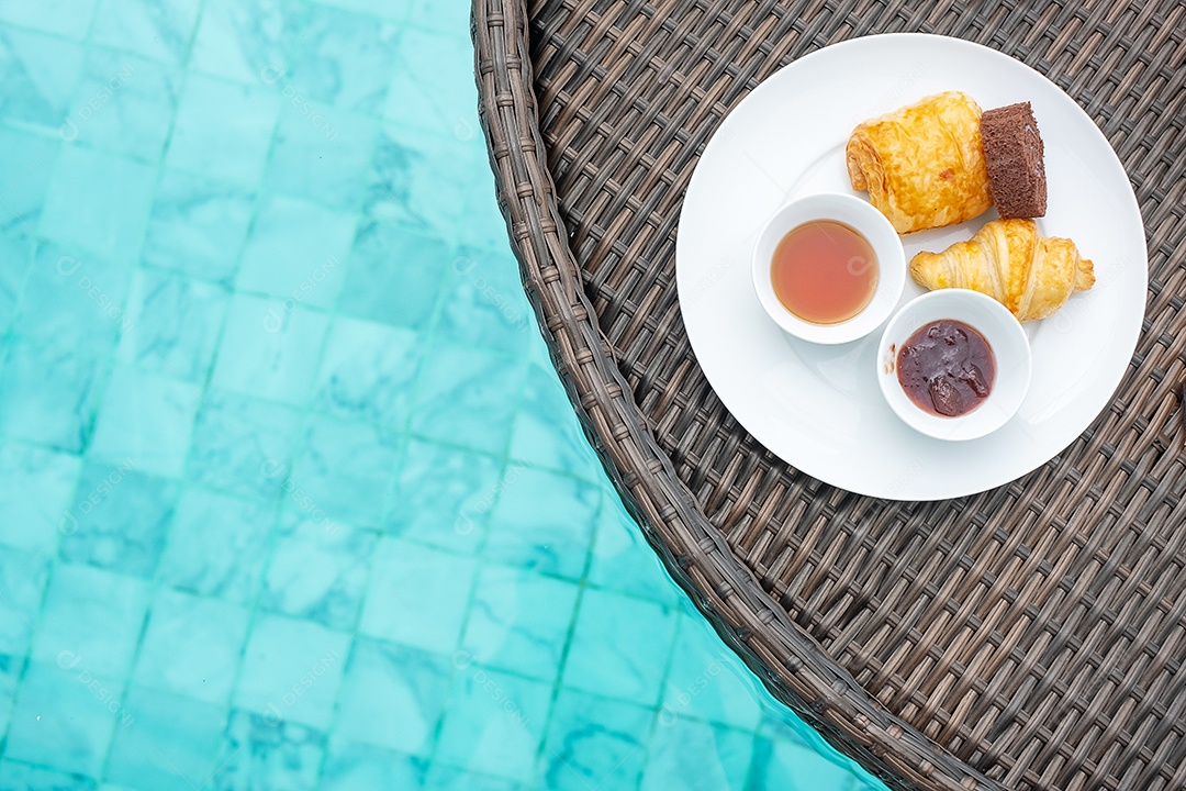 Bandeja flutuante de café da manhã na piscina no hotel de luxo ou villa de resort tropical, sobremesas; croissant, rocambole de chocolate, torta e suco de laranja. Viagens exóticas de verão, férias e conceito de férias