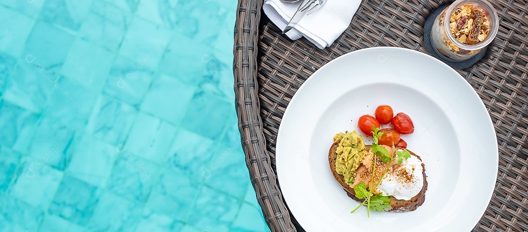 Bandeja flutuante de café da manhã na piscina no hotel de luxo ou villa de resort tropical; salmão defumado com abacate, tomate assado, ovo escalfado, pão torrado e gergelim e iogurte. conceito de viagens de verão