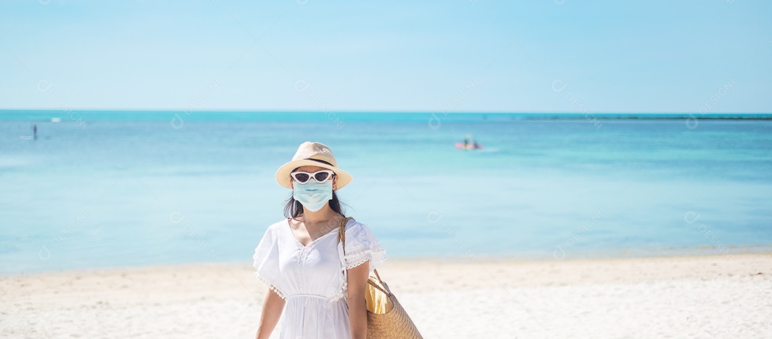 Mulher turista feliz usando máscara cirúrgica desfruta de belo mar e areia branca na praia tropical. proteção infecção por doença de coronavírus (Covid-19). Novo Normal, viagem, férias e feriado