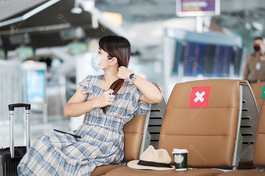 Jovem mulher usando máscara facial e usando smartphone móvel no aeroporto, proteção contra infecção por doença de coronavírus (Covid-19), viajante asiática sentada na cadeira. Novo normal e distanciamento social