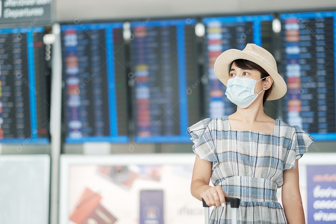 Jovem mulher usando máscara facial com bagagem verificando o tempo de voo no aeroporto, proteção contra infecção por doença de coronavírus, viajante asiática pronta para viajar. Novo Normal e viagens sob COVID-19