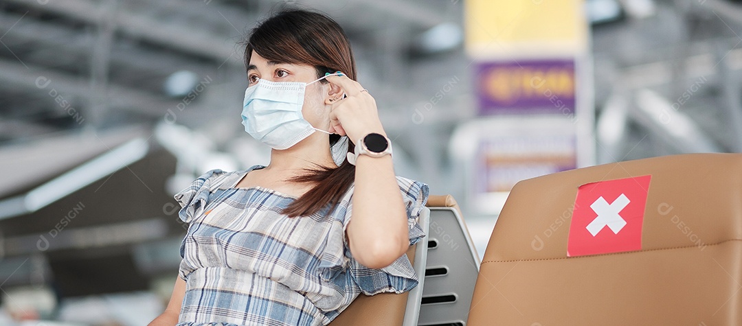 Jovem mulher usando máscara facial no terminal do aeroporto, proteção contra infecção por doença de coronavírus (Covid-19), viajante asiática sentada na cadeira. Novo conceito de viagem normal, distanciamento social e segurança