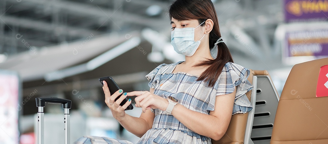 Jovem mulher usando máscara facial e usando smartphone móvel no aeroporto, proteção contra infecção por doença de coronavírus (Covid-19), viajante asiática sentada na cadeira. Novo normal e distanciamento social