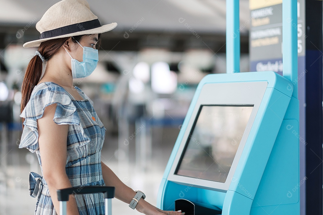 Mulher usando máscara facial médica e usando a máquina de auto check-in no terminal do aeroporto recebendo o cartão de embarque, viajante asiática pronta para viajar. Novo Normal e viagens de segurança sob COVID-19