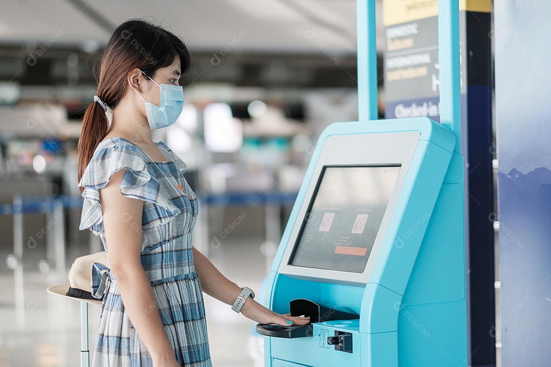 Mulher usando máscara facial médica e usando a máquina de auto check-in no terminal do aeroporto recebendo o cartão de embarque, viajante asiática pronta para viajar. Novo Normal e viagens de segurança sob COVID-19