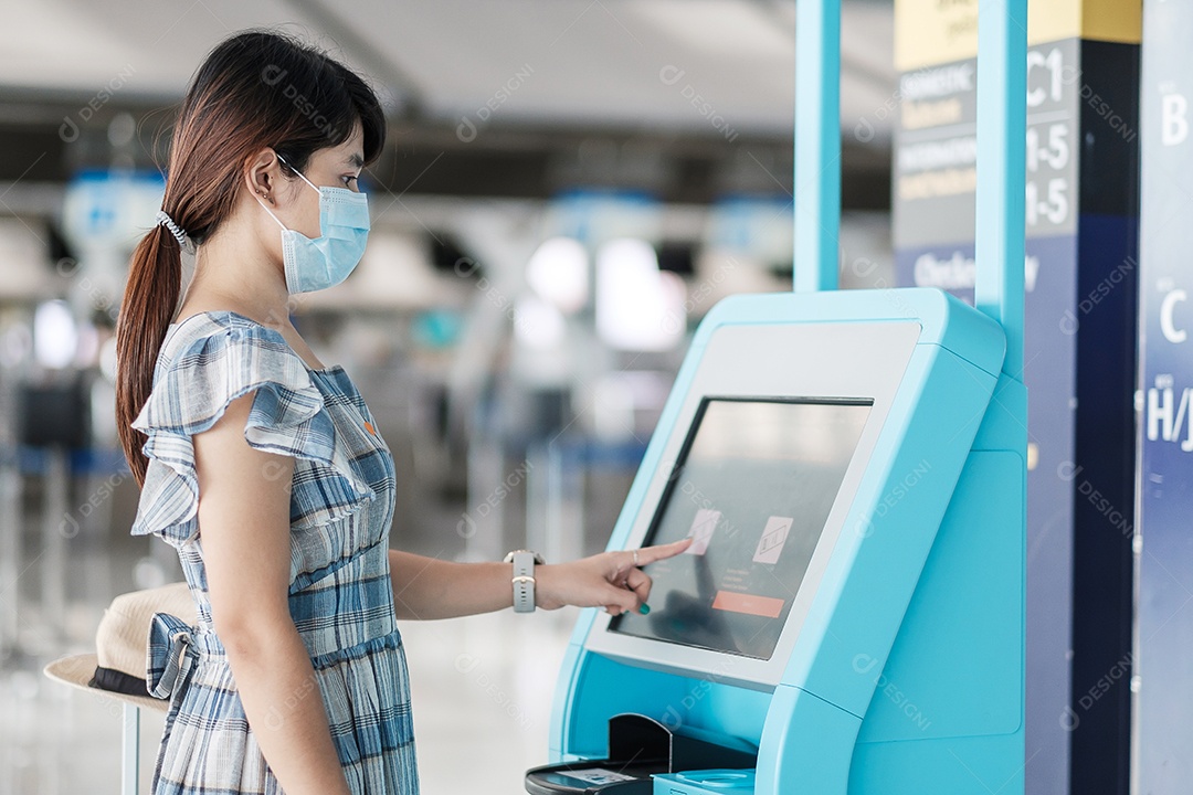 Mulher usando máscara facial médica e usando a máquina de auto check-in no terminal do aeroporto recebendo o cartão de embarque, viajante asiática pronta para viajar. Novo Normal e viagens de segurança sob COVID-19