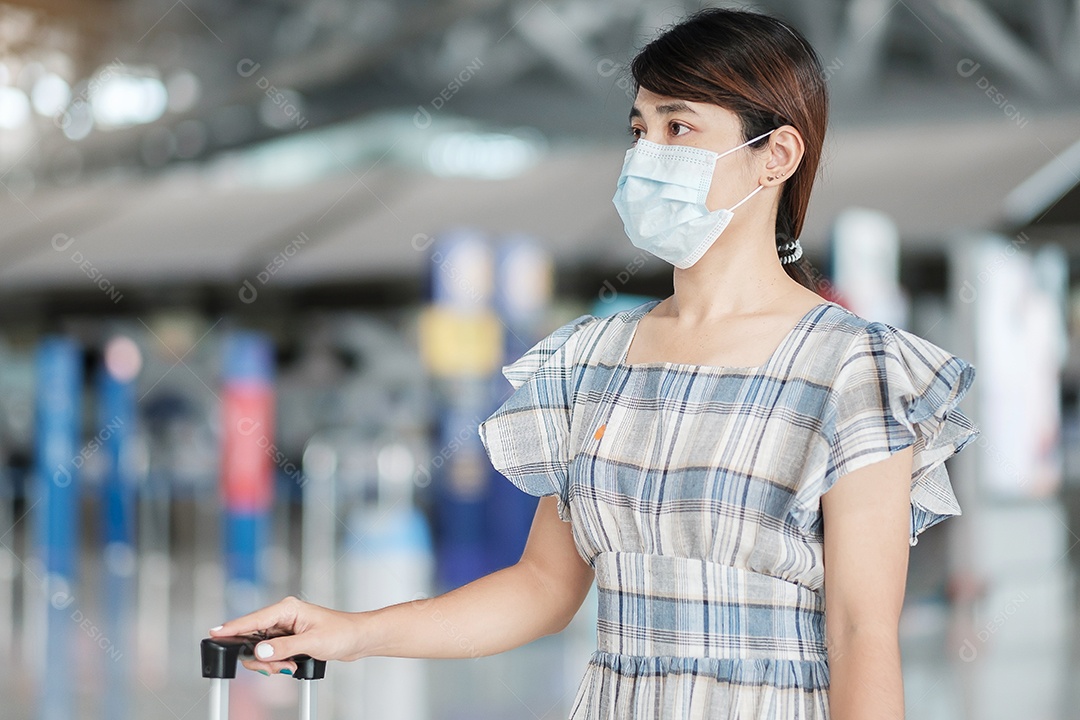 Jovem mulher usando máscara facial com bagagem verificando o tempo de voo no aeroporto, proteção contra infecção por doença de coronavírus, viajante asiática pronta para viajar. Novo Normal e viagens sob COVID-19
