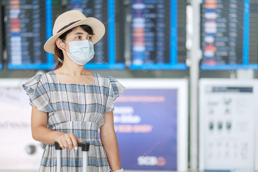 Jovem mulher usando máscara facial com bagagem verificando o tempo de voo no aeroporto, proteção contra infecção por doença de coronavírus, viajante asiática pronta para viajar. Novo Normal e viagens sob COVID-19