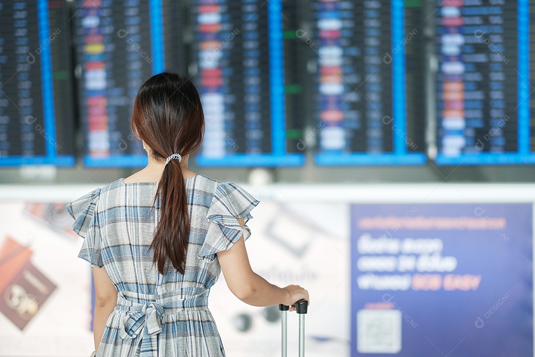 Viajante jovem verificando o tempo de voo, passageiro asiático com chapéu olhando para placa de informações no terminal do aeroporto internacional. Viagem, viagem, férias de verão e conceito de dia mundial do turismo