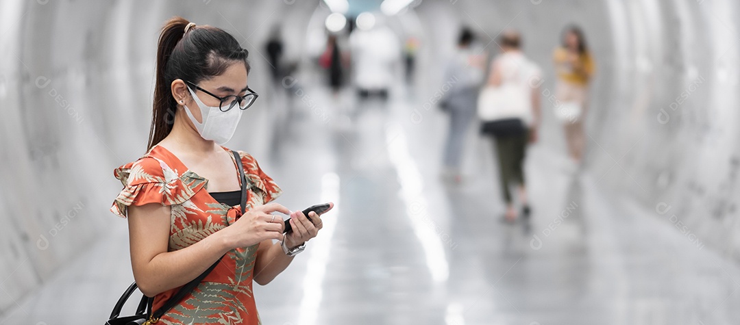 Jovem garota asiática usando máscara facial cirúrgica protege a inflexão de coronavírus, turista feliz usando smartphone durante a caminhada na estação de metrô. novo normal e vida após a pandemia de covid-19