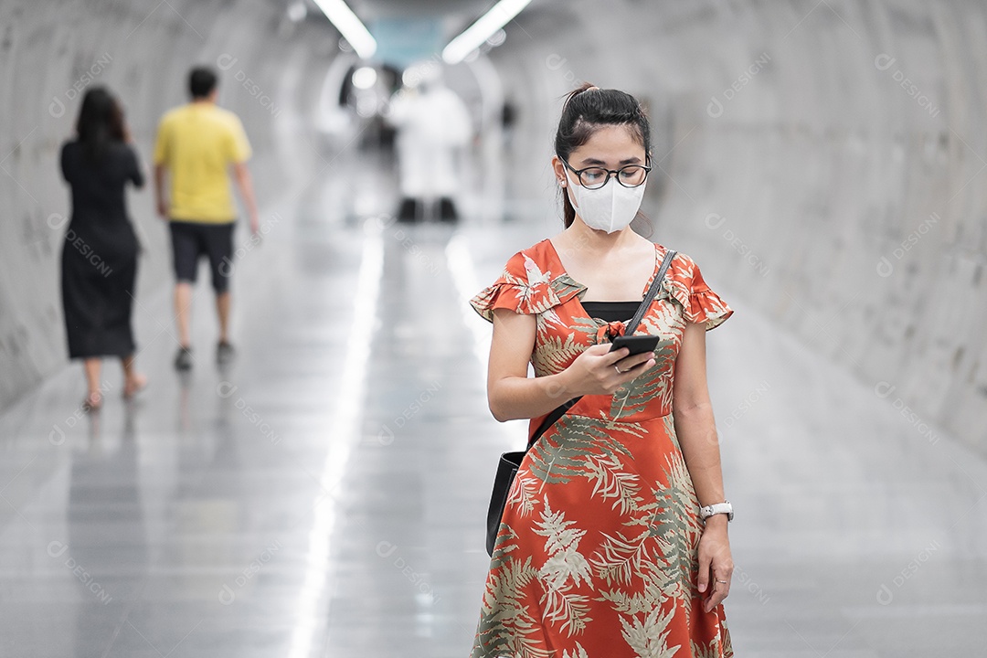 Jovem garota asiática usando máscara facial cirúrgica protege a inflexão de coronavírus, turista feliz usando smartphone durante a caminhada na estação de metrô. novo normal e vida após a pandemia de covid-19