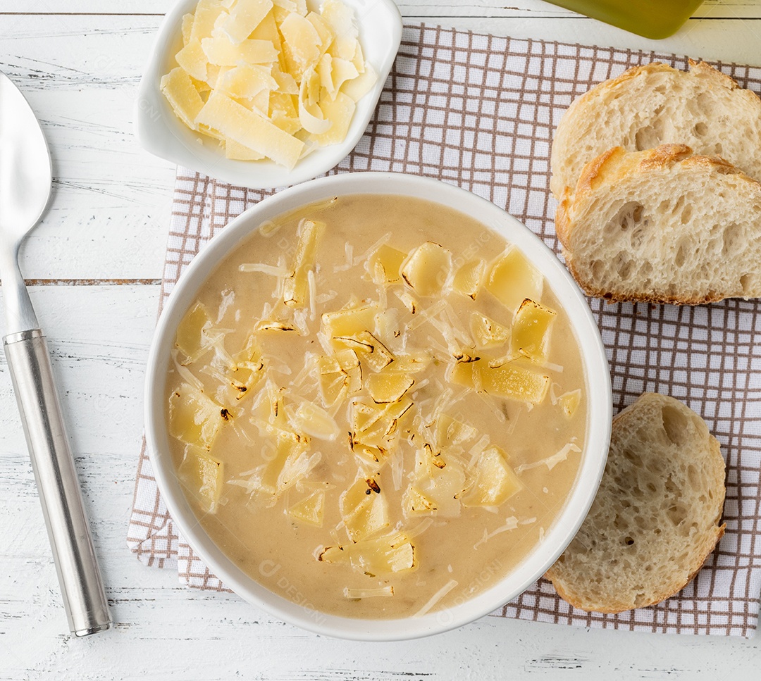 Sopa de cebola com queijo em uma tigela com fatias de pão e temperos sobre a mesa de madeira.